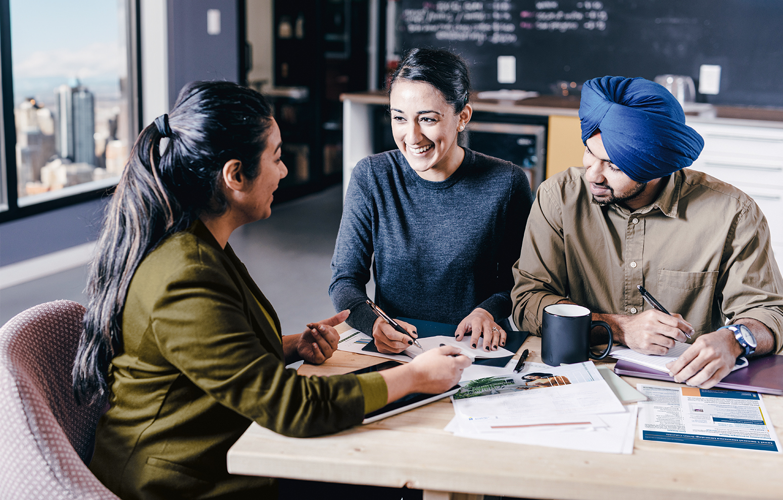 Three colleagues chat over documents at large table