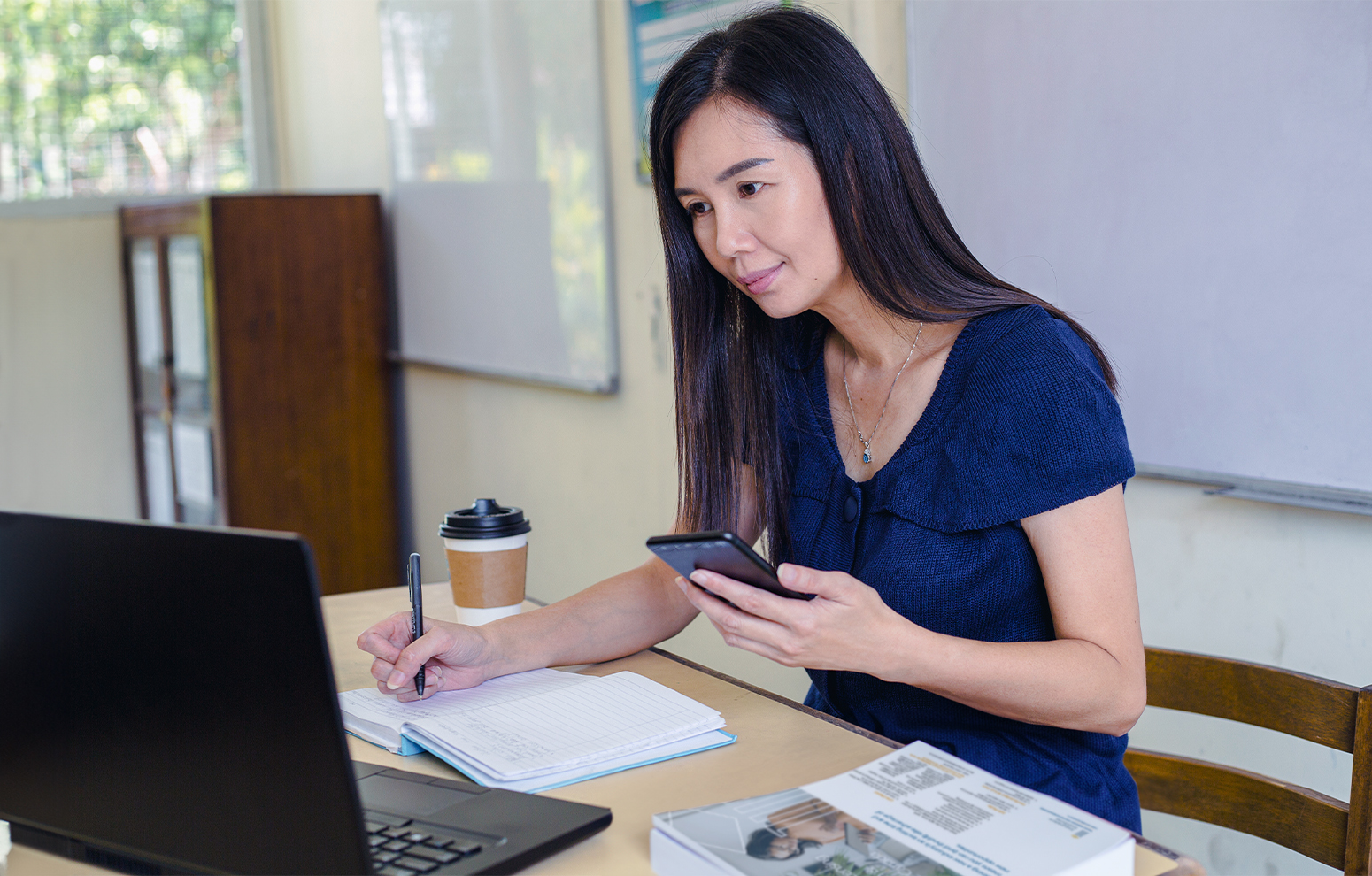 Instructor works at desk checking phone against laptop screen