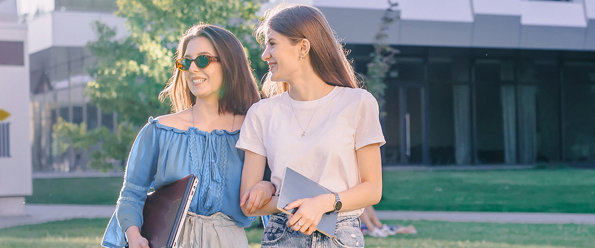 Two ladies hold tablet and laptop on outdoor walk