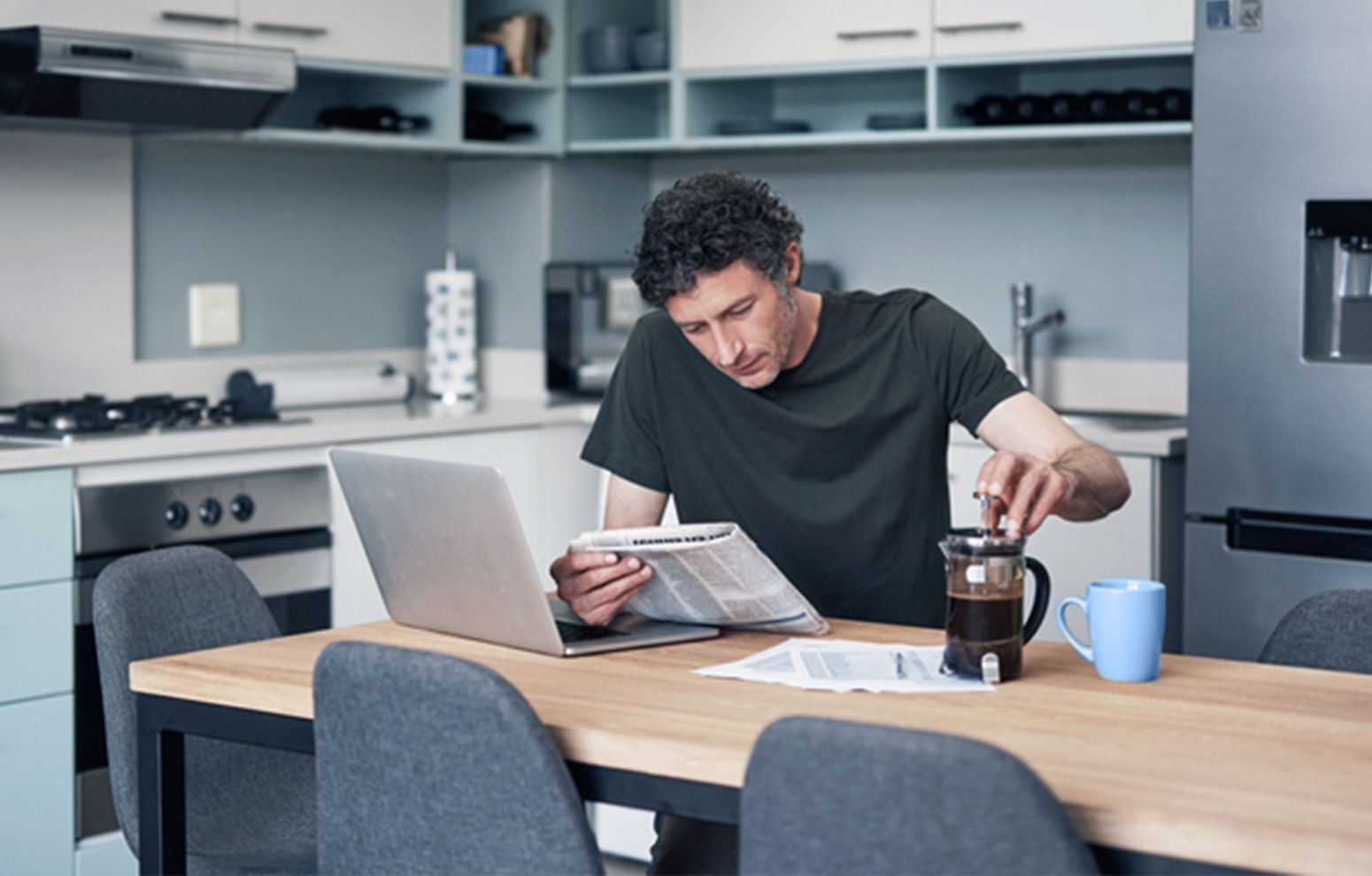 Man reads newspaper while brewing coffee at dining table