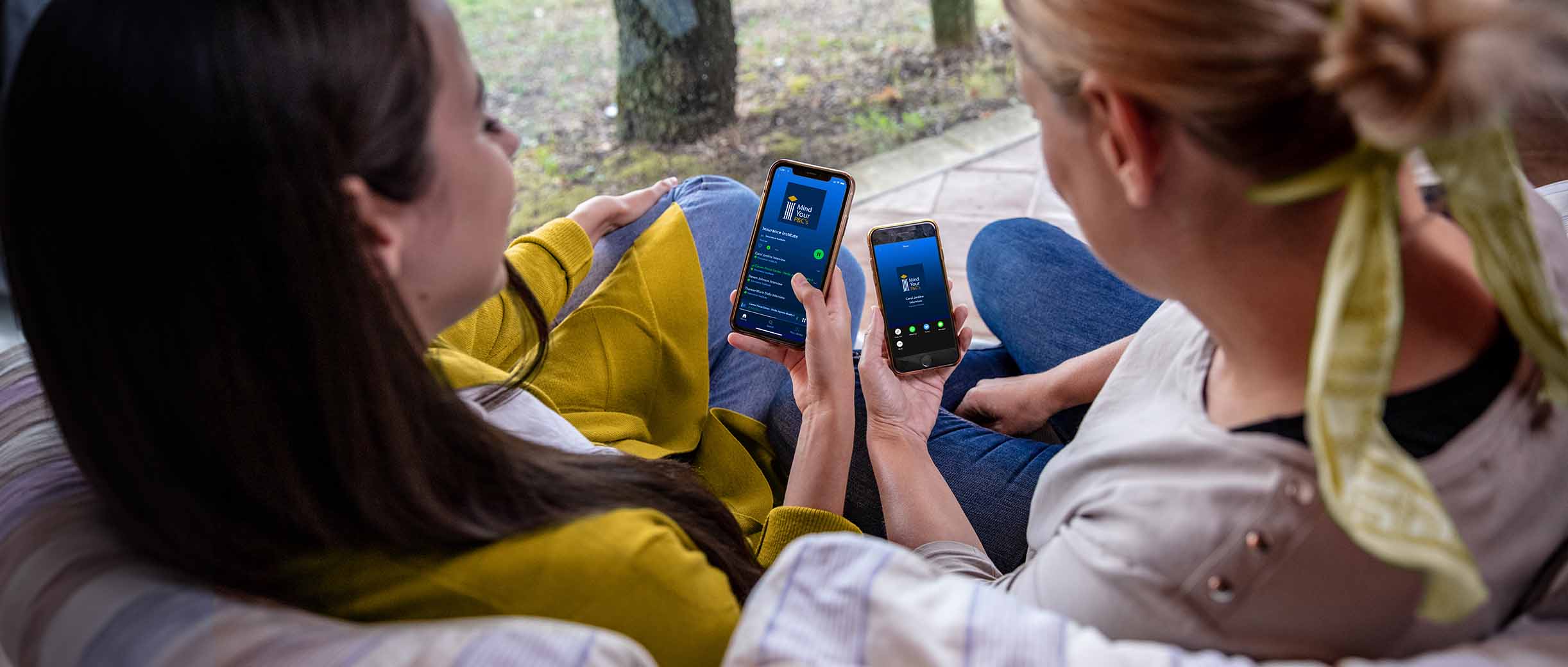 Two women sitting outside looking at cellphones. 