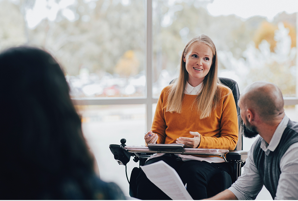 Woman sits in a wheel chair at a work meeting.