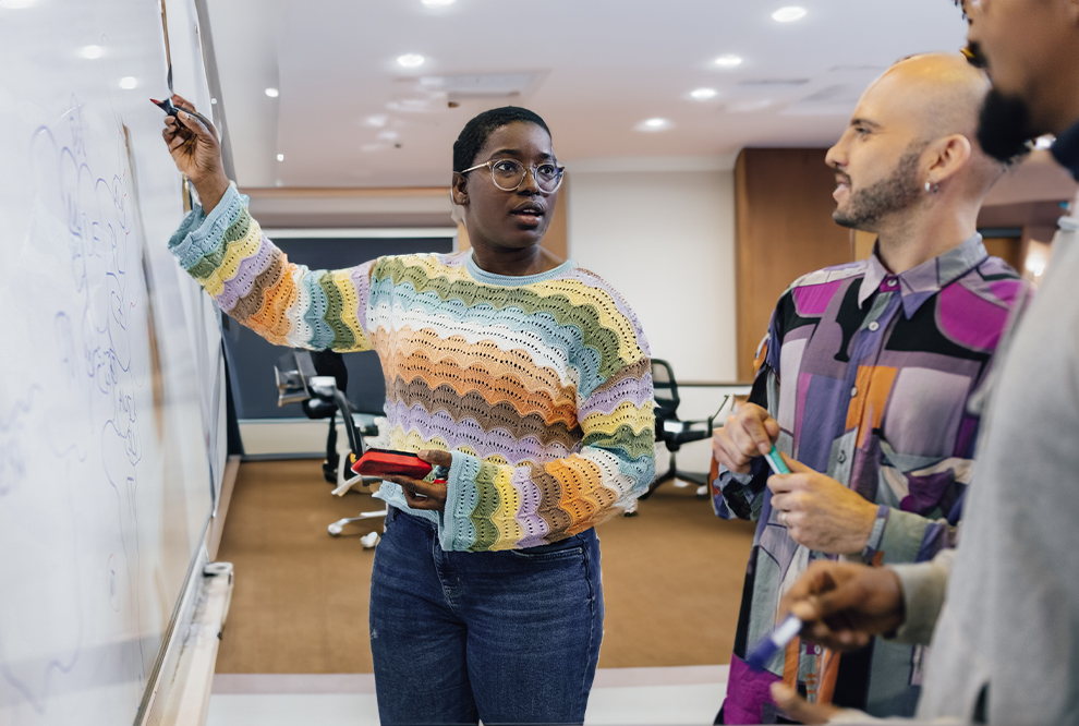 Woman works on whiteboard while coworkers watch.