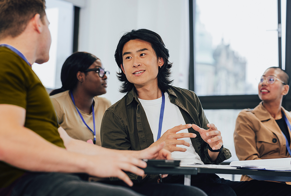 Two men talk while sitting in a classroom.