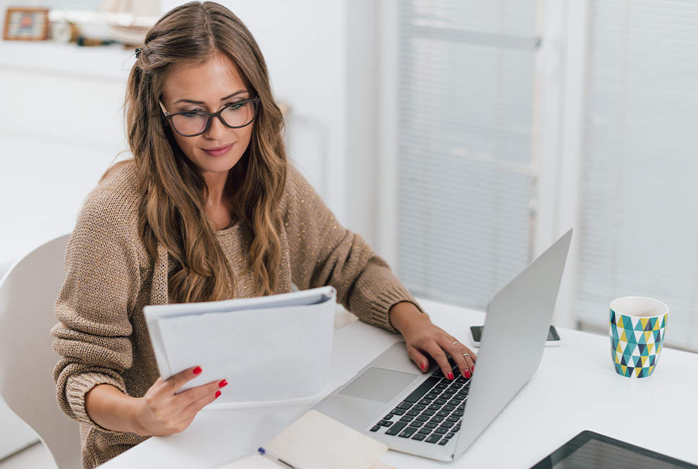 Une femme examine un document tout en utilisant l'ordinateur.