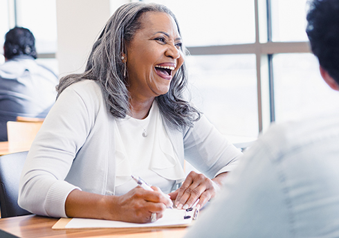 Woman sits at table with others laughing
